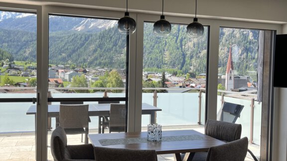 A modern dining room with a table and upholstered chairs. Through large windows, there is a view of the mountains and the surroundings. - BLANKA'S Apart Auszeit - Umhausen