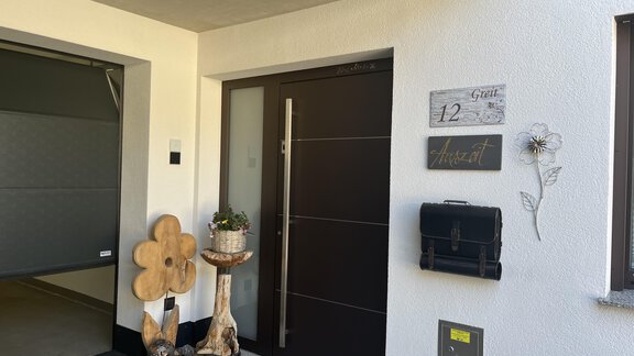 A modern house entrance with a beautiful wooden root and a mailbox. The door has a stylish handle and a house number. - BLANKA'S Apart Auszeit - Umhausen