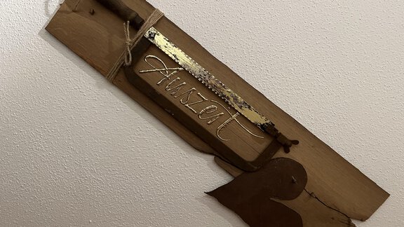 Ein dekoratives Holzbrett mit einer Klinge und der eingravierten Aufschrift "Auszeit". Daneben befindet sich ein herzförmiges Element aus Metall. - BLANKA'S Apart Auszeit - Umhausen