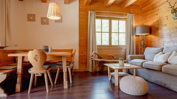 A cozy living space with wooden details and a large window. There is a dining area, a sofa, and decorative elements that create a warm atmosphere. - Chalet Carla - Umhausen