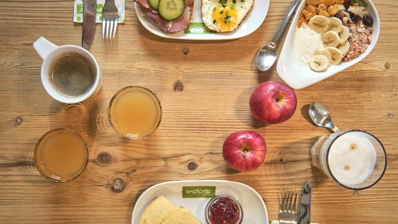 Ein reichhaltiges Frühstück mit verschiedenen Tellern. Auf den Tellern sind Eierspeisen, Schinken, Brot, Obst und Müsli zu sehen. - Explorer Hotel Ötztal - Umhausen