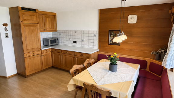 A cozy kitchen with wooden cabinets and a small dining area. A table with a tablecloth and a flower vase is the centerpiece of the room. - Ferienhaus am Spielroan - Umhausen