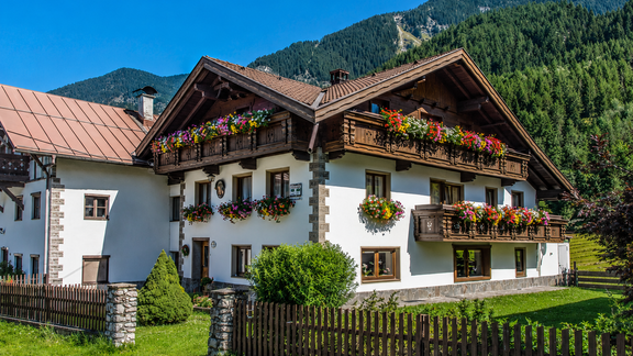 A traditional alpine house with colorful flower boxes. In the background, green mountains and a blue sky can be seen. - Ferienhaus am Spielroan - Umhausen