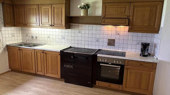 A modern kitchen with wooden cabinets and white tiled wall. There is a stove, a refrigerator, and a sink, all in a bright room. - Ferienhaus am Spielroan - Umhausen
