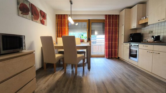 A modern kitchen with a dining table and four chairs. The walls are bright, and large windows bring plenty of light into the room. - Ferienwohnung Martha - Umhausen