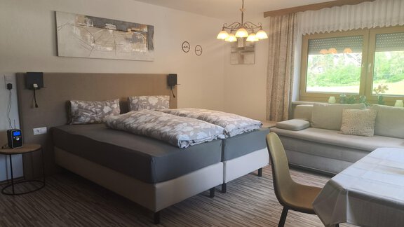 A cozy sleeping area with two beds and a modern sofa. Large windows provide plenty of daylight and a pleasant atmosphere. - Ferienwohnung Martha - Umhausen