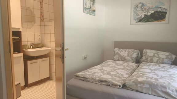 A cozy bedroom with a double bed and a modern decor. In the background, a bathroom with a sink and mirror can be seen. - Ferienwohnung Martha - Umhausen