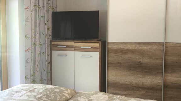 A cozy bedroom with a double bed and floral bedding. The room features a television and a modern wardrobe. - Ferienwohnung Martha - Umhausen
