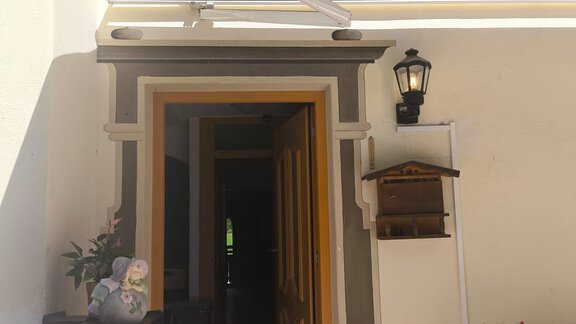 An inviting entrance with an open door and a pleasant outdoor area. Next to the door, there are flowers and a small lamp. - Ferienwohnung Martha - Umhausen