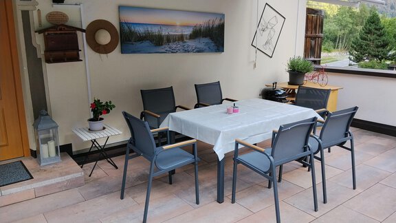 A cozy terrace with a table and six chairs. In the background, there is a picture of a landscape and some green plants. - Ferienwohnung Martha - Umhausen