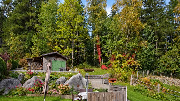 A beautiful garden with colorful flowers and large stones. In the background, trees in various colors and a small hut can be seen. - Ferienwohnung Martha - Umhausen