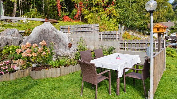 A sunny garden with a table and several chairs.  
Surrounded by blooming plants and rocks. - Ferienwohnung Martha - Umhausen