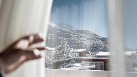 Ein Blick durch das Fenster auf verschneite Berge und kleine Häuser. Die Landschaft ist idyllisch und winterlich. - MYALPS Ötztal - Umhausen