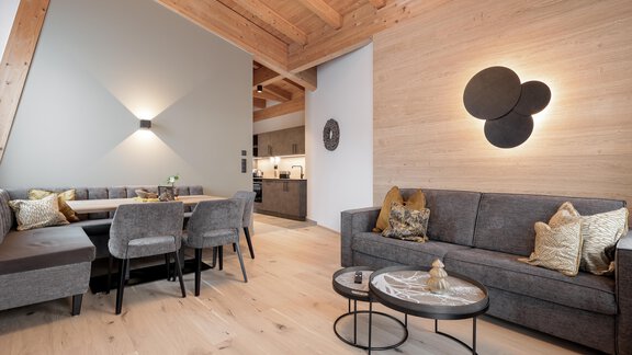 Ein modernes Wohnzimmer mit einem grauen Sofa und einem Esstisch. Die Wände sind in sanften Farbtönen gehalten, und die Holzdecke verleiht eine gemütliche Atmosphäre. - MYALPS Ötztal - Umhausen