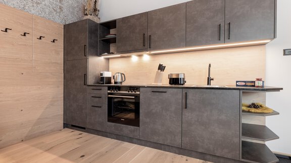 Eine moderne Küche mit dunklen Schränken und eleganter Beleuchtung. Der Boden besteht aus Holz und es gibt verschiedene Küchengeräte. - MYALPS Ötztal - Umhausen