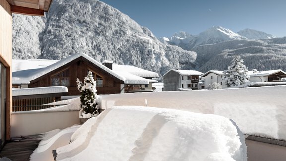 Eine winterliche Landschaft mit schneebedeckten Dächern und Bergen im Hintergrund. Der Himmel ist klar und blau. - MYALPS Ötztal - Umhausen