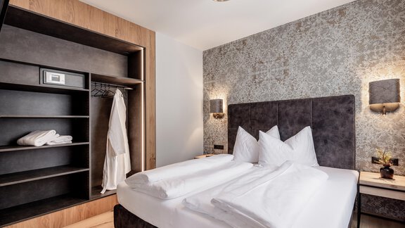Ein modernes Hotelzimmer mit einem großen Bett, eleganter Bettwäsche und einem stilvollen, neutralen Farbschema. Im Hintergrund befinden sich ein Kleiderschrank und eine gemütliche Beleuchtung. - MYALPS Ötztal - Umhausen
