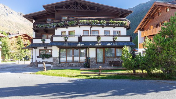 A charming multi-story building with wooden decorations and balconies.  
Surrounded by green trees and mountains. - Garni Stefani - Vent