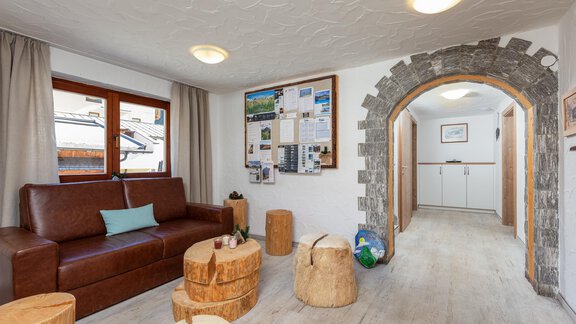 A cozy living area with a leather couch and wooden stools. In the background, you can see an entryway with an architectural archway opening. - Garni Stefani - Vent