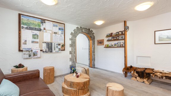 A bright reception room with rustic furnishings.  
Wood logs serve as seating, and information and photos hang on the wall. - Garni Stefani - Vent