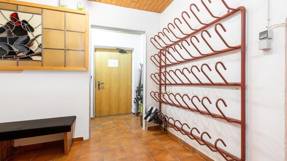 An entrance area with a wooden shelf and a large coat rack on the wall. The floor is covered with brown tiles and there is a wooden bench. - Garni Stefani - Vent