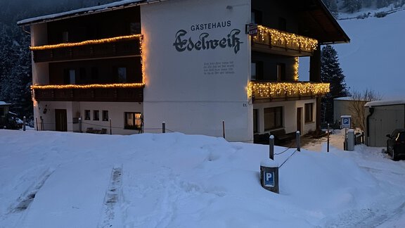 A cozy building in the snow, festively decorated with lights. In the background, snow-covered mountains and a misty atmosphere can be seen. - Gästehaus Edelweiss - Vent