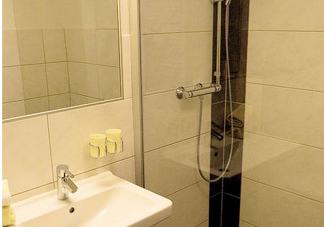 A modern bathroom with a glass shower and a sink. The walls are light tiled and there are toiletries on the sink. - Gästehaus Soldanella - Vent