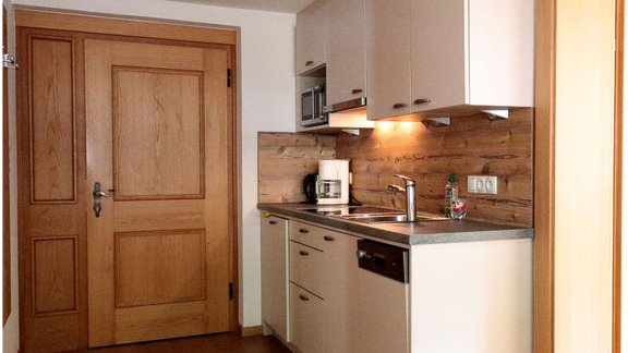 A modern kitchen with light cabinets and a wooden cladding. The equipment includes a stove, a sink, and a coffee maker. - Gästehaus Soldanella - Vent