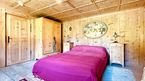 A cozy bedroom with wood paneling and a large bed in purple. The room has a warm atmosphere and a rustic interior design. - Haus Freistabl - Vent