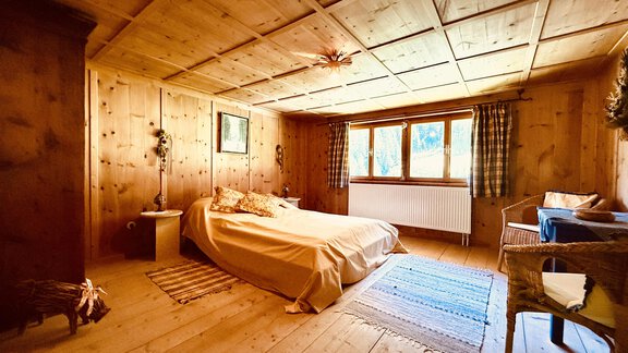 A cozy wooden bedroom with warm tones. There is a large window that lets in natural light. - Haus Freistabl - Vent