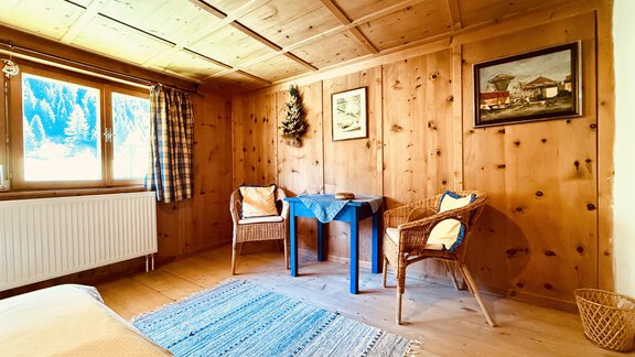 A cozy room with wooden walls and a large window. In the room, there are two chairs, a table, and a rug. - Haus Freistabl - Vent