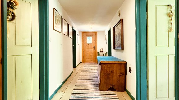 A bright hallway with a colorful carpet and open doors on both sides. The walls are painted in soft colors and there are natural light sources. - Haus Freistabl - Vent