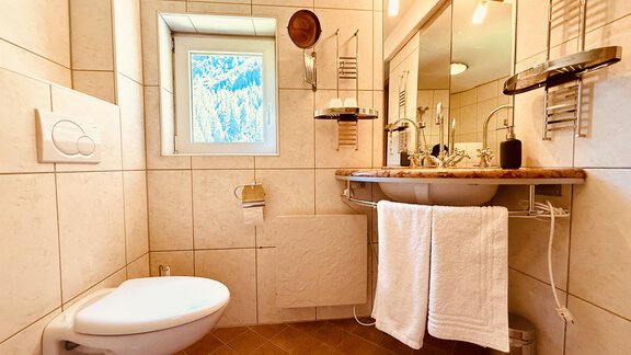 A modern bathroom with bright tiles and a large mirror. On the sink shelf, there are towels, and a small window offers a view outside. - Haus Freistabl - Vent
