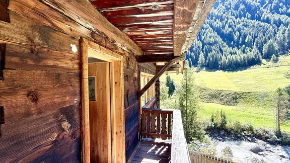 A cozy wooden balcony overlooking a green meadow and wooded mountains. Nature surrounds the house, creating a peaceful atmosphere. - Haus Freistabl - Vent