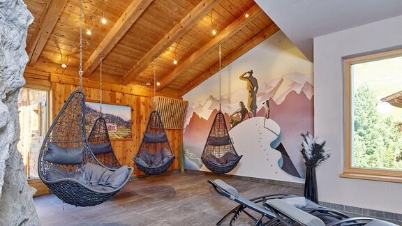 A modernly furnished room with hanging swings and an artistic mural. The room has warm wooden ceilings and large windows that let in plenty of light. - Hotel Vent - Vent
