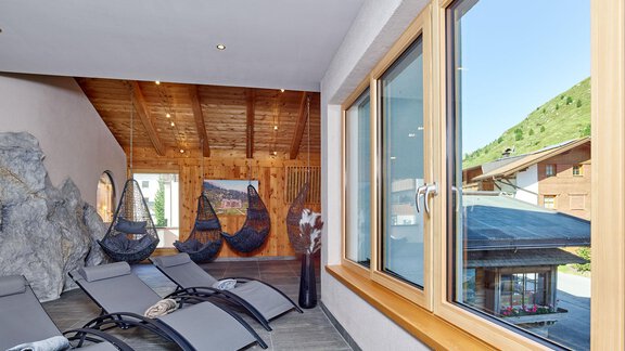A modern wellness area with lounge chairs and large windows. The view shows a green landscape and wooden architecture. - Hotel Vent - Vent