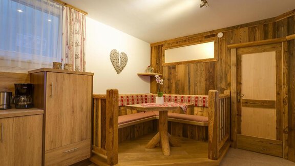 A cozy dining area with wood paneling and a typical seating area. The room has a warm ambiance with a small table and flowers. - Apart Praxmarer - Zwieselstein