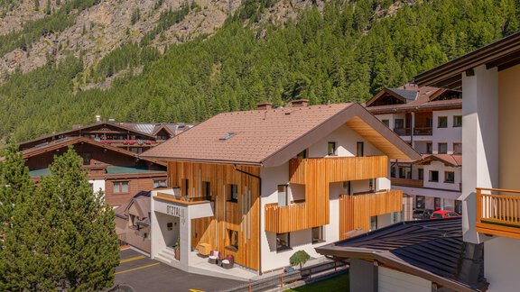 A modern house with wooden cladding in a picturesque mountain landscape. Surrounded by green trees and traditional chalets. - Garni Ötztal ROOMS & APARTS - Zwieselstein