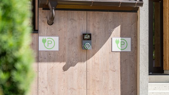 A wall with two parking symbols for electric vehicles and a charger. The surface is made of wood and the surroundings appear modern and inviting. - Garni Ötztal ROOMS & APARTS - Zwieselstein