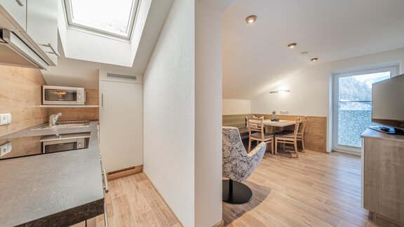 A modern furnished kitchen with a light wooden floor. In the background, there is a dining area with a table and chairs. - Garni Ötztal ROOMS & APARTS - Zwieselstein