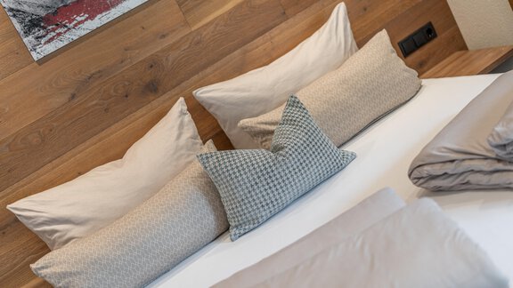 A cozy bedroom with a bed and several pillows. The walls are made of wood and there are decorative elements in the background. - Garni Ötztal ROOMS & APARTS - Zwieselstein