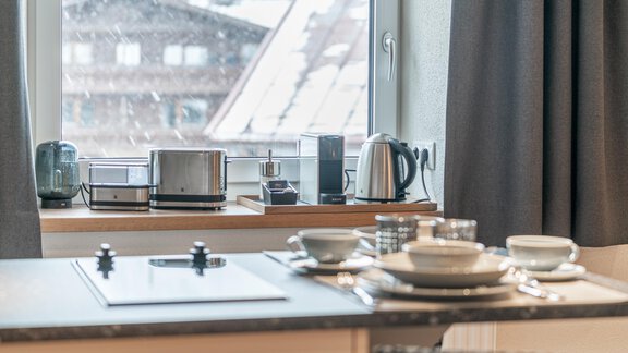 A modern kitchen with a window overlooking a residential building. Kitchen appliances and dishes are on the countertop. - Garni Ötztal ROOMS & APARTS - Zwieselstein