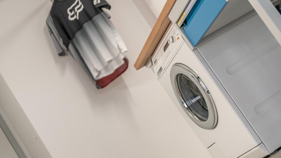 A laundry room with a washing machine and a dryer. Two T-shirts hang on the wall. - Garni Ötztal ROOMS & APARTS - Zwieselstein