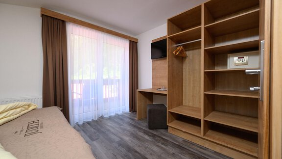 A bright room with a large window and curtains. There is a shelf, a TV, and a table. - Gästehaus Judith - Zwieselstein