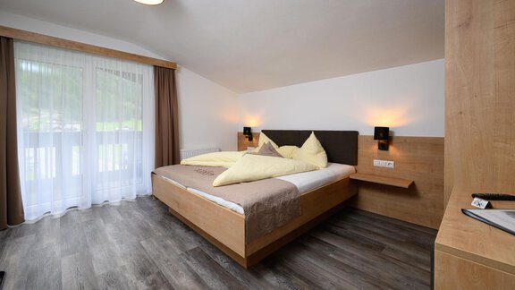 A modern bedroom with a double bed and wooden furniture. Large windows provide plenty of daylight. - Gästehaus Judith - Zwieselstein