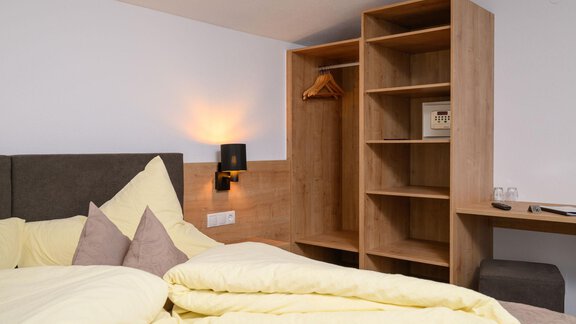 A cozy bedroom with a large bed and yellow comforters. The room contains a wooden wardrobe and a small table surface. - Gästehaus Judith - Zwieselstein