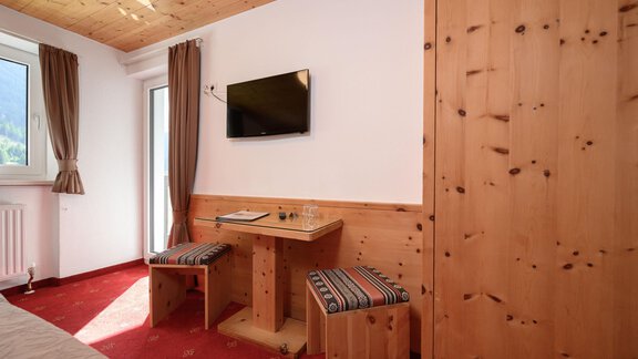 A cozy room with wooden details and a television on the wall. There is a small table and two chairs that invite relaxation. - Gästehaus Judith - Zwieselstein