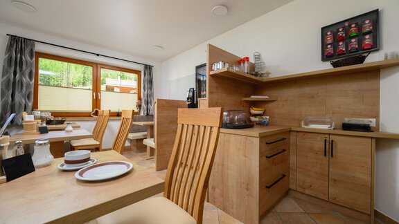 A bright kitchen with wooden shelves and modern furniture. Plates and cups are set on the table for breakfast. - Gästehaus Judith - Zwieselstein