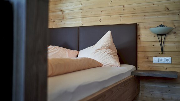 A cozy bedroom with wooden interior. The bed is furnished with soft pillows and blankets. - Gästehaus Judith - Zwieselstein