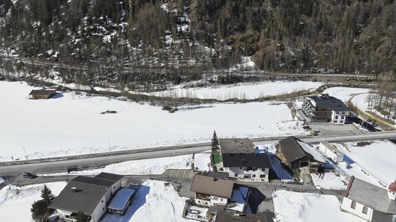 A peaceful winter landscape with snow-covered houses and a snow-covered area. In the background, tall trees can be seen. - Gästehaus Judith - Zwieselstein